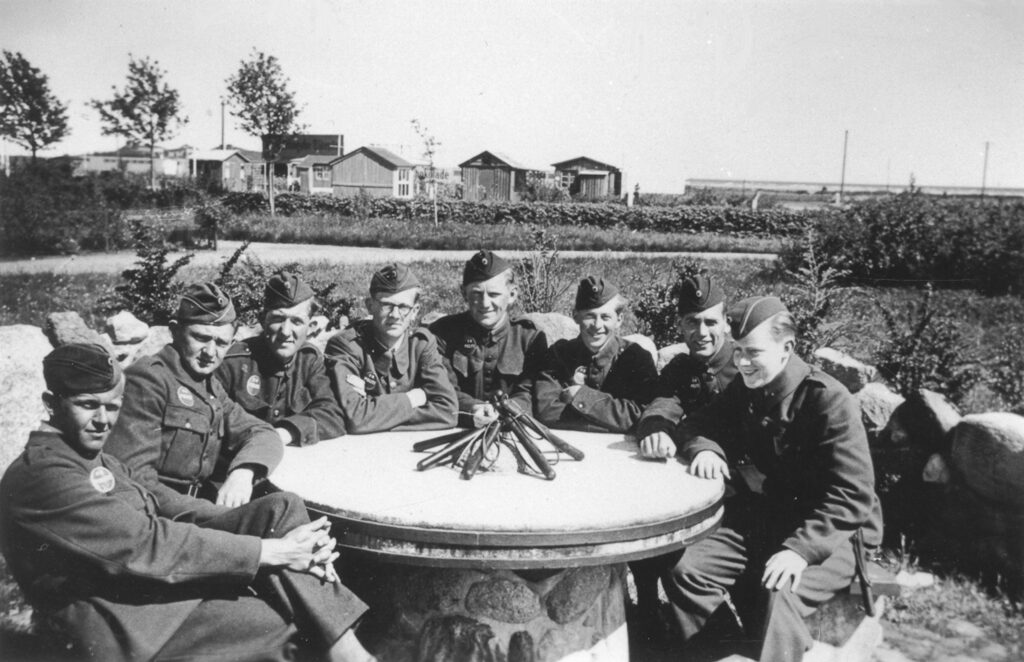 1941. CB-betjente, der var stationeret på Dragør Skole, slapper af i Wieders Anlæg. I baggrunden kolonihaverne og Arne Jacobsens Badeetablissement. Museum Amager, Dragør Lokalhistoriske Arkiv.