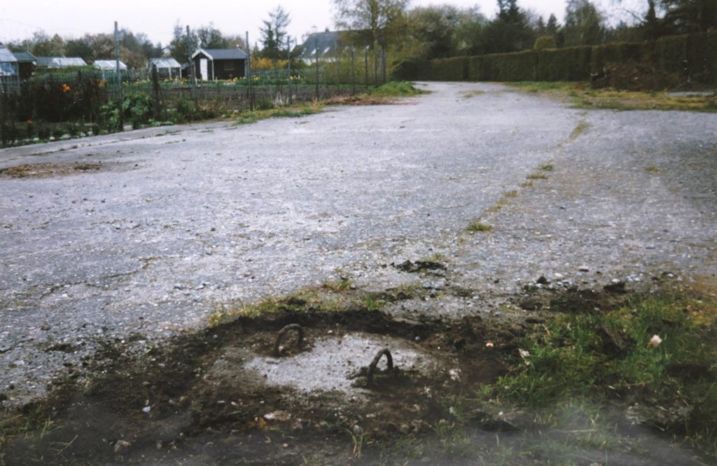 Maj 1992. Rullevejen der blev brugt som tilkørselsvej til havekolonien. Midt på den 12 meter brede betonvej var der med passende mellemrum 1 meter dybe bombebrønde. I tilfælde af allieret forsøg 1944-45 på at overtage Københavns Lufthavn samt omliggende rullebaner, skulle alle baner sprænges. To mand kunne anbringe flybomber i brøndene og antænde. Sådanne brønde findes flere steder. Bl.a. på Rytterager ulige numre midt på den nu asfalterede betonvej. Foto: Dines Bogø.